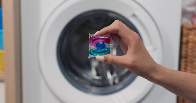Close-up of hands holding a soft laundry capsule against the backdrop of a washing machine.