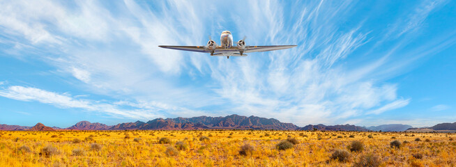 Old metallic propeller airplane in the sky - Panoramic view of desert plains in Namibia Africa with hills and mountains in the background