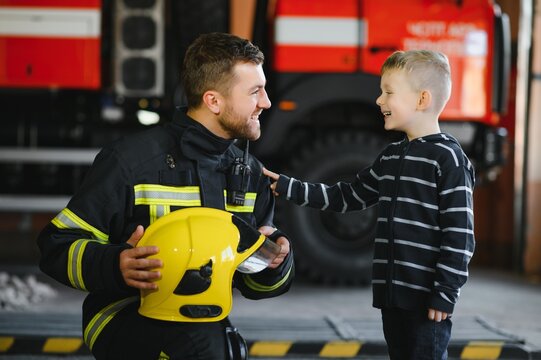 A firefighter take a little child boy to save him. Fire engine car on background. Fireman with kid in his arms. Protection concept.