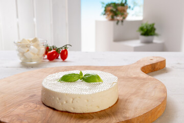 fresh cheese with basil leaf on wooden cutting board resting on a white wooden table, set