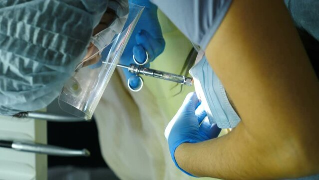 Boy with his eyes covered under general anesthesia while professional dental treatment is performing. Vertical footage. Dental clinic with modern procedures. Doctor hands taking syringe. 4 k video