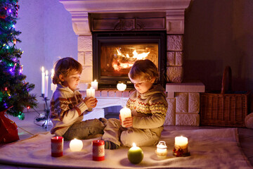 Cute toddler boys, blond twins playing together and lookinig on fire in chimney. Family celebrating...