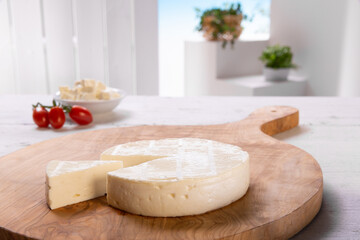 fresh cheese with tomatoes on wooden cutting board resting on a white wooden table, set