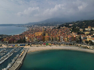 Fototapeta na wymiar Aerial view of Menton in French Riviera from above. Drone view of France Cote d'Azur sand beach beneath the colorful old town of Menton. Small color houses near the border with Italy, Europe.