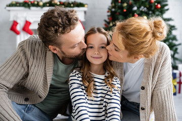 Parents kissing happy daughter during christmas at home