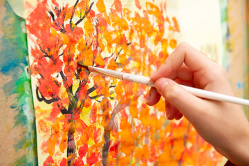 Young artist paints orange autumn trees on canvas