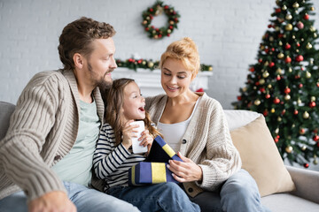 Smiling woman opening gift box with smartphone during christmas at home