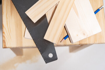 Carpentry saw and pencil tools lie next to wooden boards and slats.