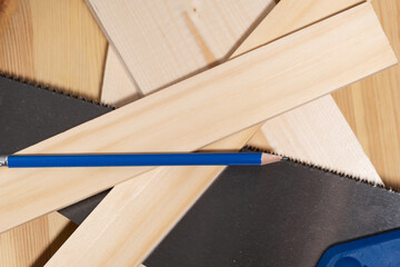 The pencil lies on the saw and wooden boards and slats, carpentry work