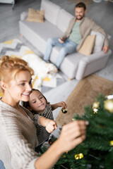 High angle view of girl pointing at christmas tree near mom at home
