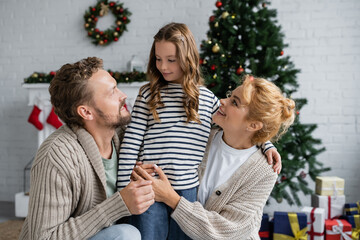 Smiling parents in cardigans looking at daughter during christmas at home