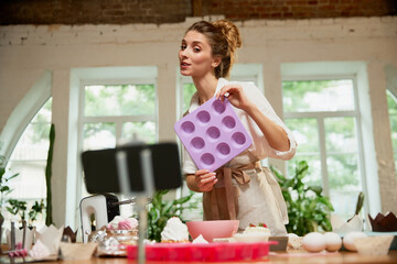 Young beautiful girl culinary specialist writes video blog on baking. Smiling female vlogger or shooting blog filming reportage advertising video
