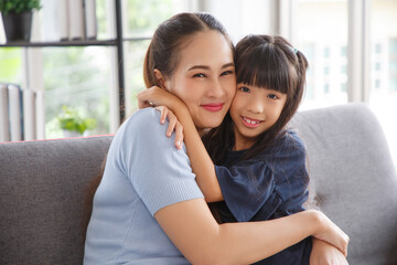 Portrait of asian daughter kissing her beautiful happy mother in living room.