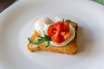 Whole wheat toasted bread with poached egg, tomato, arugula and cheese on white plate.