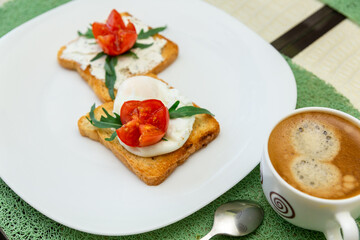 Breakfast with cup of coffee and whole wheat toasted bread with poached egg, tomato, arugula and cheese on white plate.