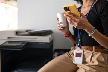 Woman sitting in the office with a phone and cup with coffee in hands