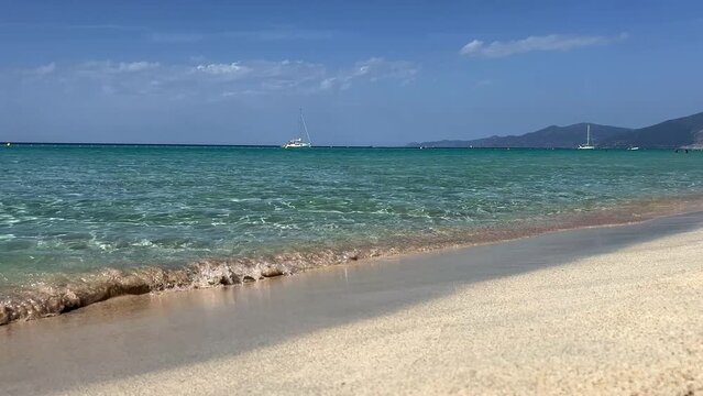 Low angle ground level pov of Saleccia idyllic sandy beach with turquoise sea water and yacths and sailboats in background in Corsica, France