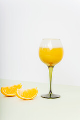 Wineglass with orange juice and orange slices on light green table. Healthy drink. Closeup
