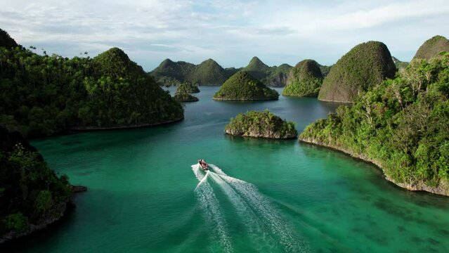 Small boat drives through in Raja Ampat Indonesia, in between tropical islands, turquoise waters, and coral reefs. Aerial Drone shot in 4K.