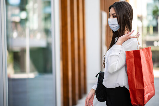 Beautiful Young Woman Shopping Bags And Walking Outdoor In A City Center Wearing A Protrctive Mask Against Covid 19 Pandemic