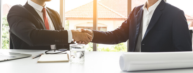 Two businessmen shaking hands after deal contract to mortgage real estate.