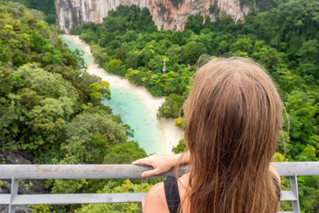 Woman on viewpoint to the beach with blue water lagoon, jungle and rocks. Female traveler on tour to exotic island. Boat trip on Hong island, Thailand. Asia tourism, vacation, holidays. Back view