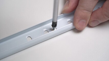 Male hands with a screwdriver screw the fittings to the furniture with a screw.