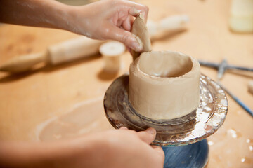 Closeup hands of female ceramis artist working at pottery studio on pottery wheel. Handcrafted products. Creative people, hobbies and skills