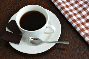 white cup of coffee with saucer, teaspoon and chocolate isolated, close-up