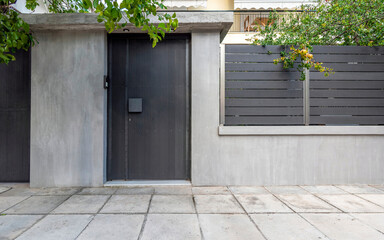 A modern house entrance, with a grey door and fence wall by the sidewalk. Athens, Greece.