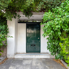 A contemporary house entrance, with dark green painted iron door and foliage by the sidewalk. Athens, Greece.