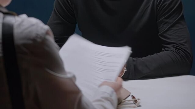 Female detective interrogates suspected criminal in handcuffs. Police officer opens dossier folder with evidence. FBI agent asks to sign papers. Arrested mafia refuses to talk to cop without lawyer