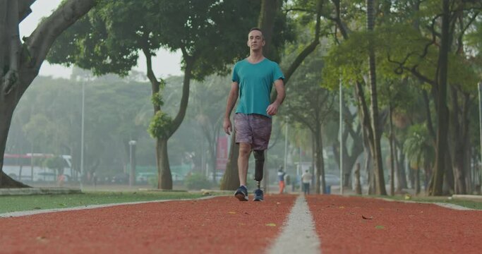 Front View Of A Middle Aged Disabled Athlete Man With Prosthetic Leg Walking Forward Toward Camera Outdoors On Running Track