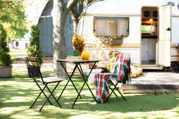 Interior cozy campsite with flowers and pumpkins. Wooden RV house porch with garden furniture. Campsite with caravan trailer in garden. Summer garden with chair and table. 