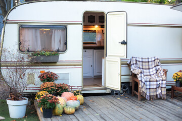 Wooden RV house porch with garden furniture. Campsite in garden. Wooden armchair near outside caravan trailer. Halloween design home. Interior cozy yard campsite with fall flowers potted and pumpkins.