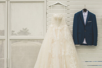 Groom suit and bridal dress hanging on white slat wall in wedding ceremony day,Luxury costume on...