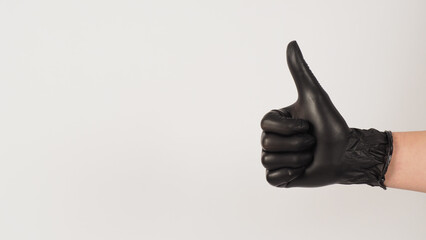 The hand is wearing a black latex glove and do like or thumbs up hand sign on white background.