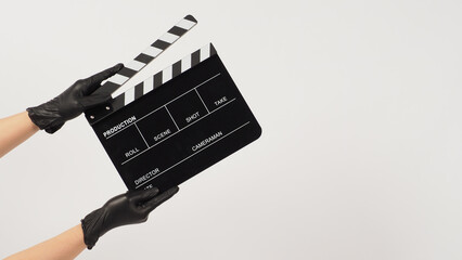 Naklejka premium Hand hold black clapper board or movie slate and wear black latex glove on white background.