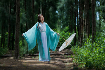 Portrait woman in a Chinese costume  with a sword in the forest. Chinese girl with a traditional...