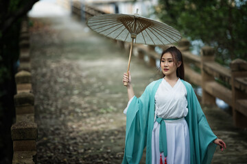Portrait woman in a Chinese costume  with a sword in the forest. Chinese girl with a traditional...