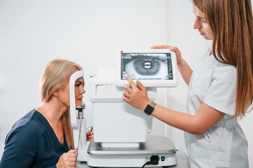 Eye is on the monitor. Woman's vision is tested by clinic worker that using special device