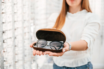 Holding case with glasses. Woman is in the store. Close up view