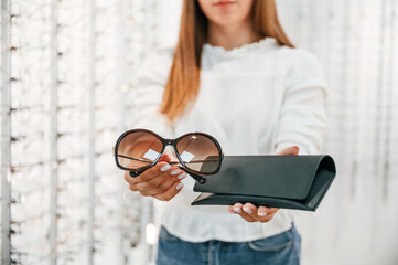 Brown colored lenses and black case. Woman holding glasses in hands in the store. Close up view