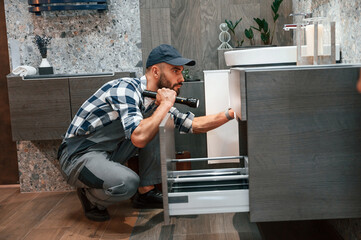 Using flashlight. Plumber in uniform is indoors at home