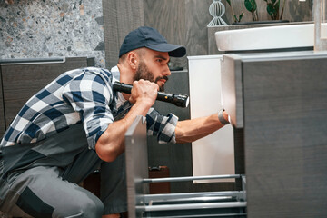 Using flashlight. Plumber in uniform is indoors at home