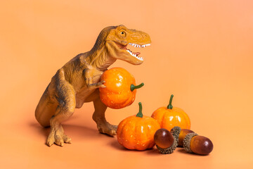Toy dinosaur Tyrannosaurus holding pumpkin in its paws, on white podium isolated on orange background Holiday greeting card Happy Halloween day, Hello Autumn creative minimal concept