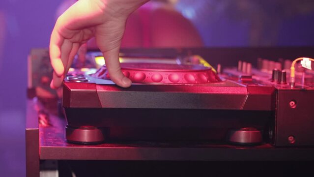 A DJ presses buttons on a professional music control panel in a nightclub. Multi-colored light music. Night life, close-up
