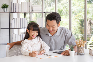 Children education and home school concept : Young asisn father pleased to see little daughters' study success. Excited smiling small child girl enjoying learning and writing with pleasant dad at home
