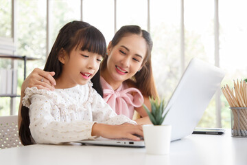 Children education and home school concept : Young asian mother pleased to see little daughters' study online. Excited smiling child girl enjoying online learning  with pleasant mom at home.