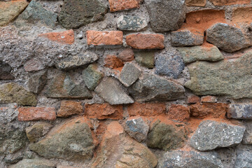 Close up detail of crumbling red bricks and rough stones on an old stone wall. Uneven, crooked, grungy texture for backgrounds. Graphic design element.